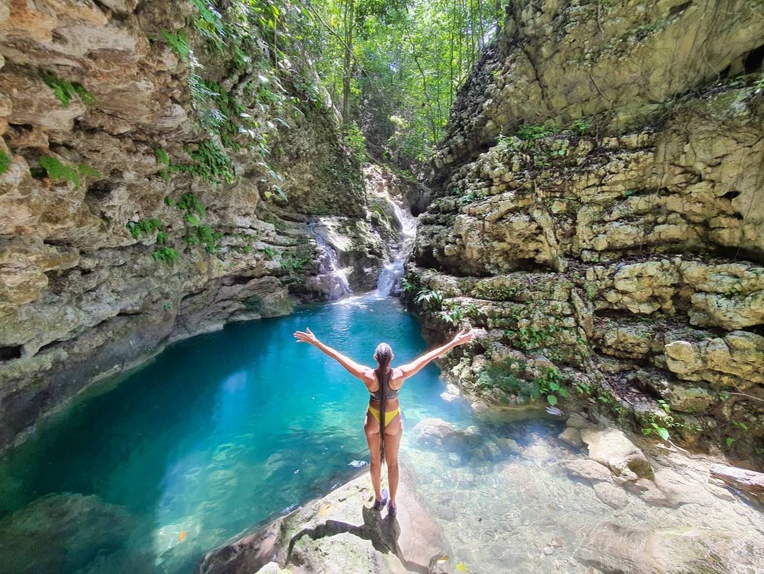 A woman spreading her arms open in front of a waterfall and natural pool during a hike, one of the things to do in Puerto Plata, Dominican Republic.