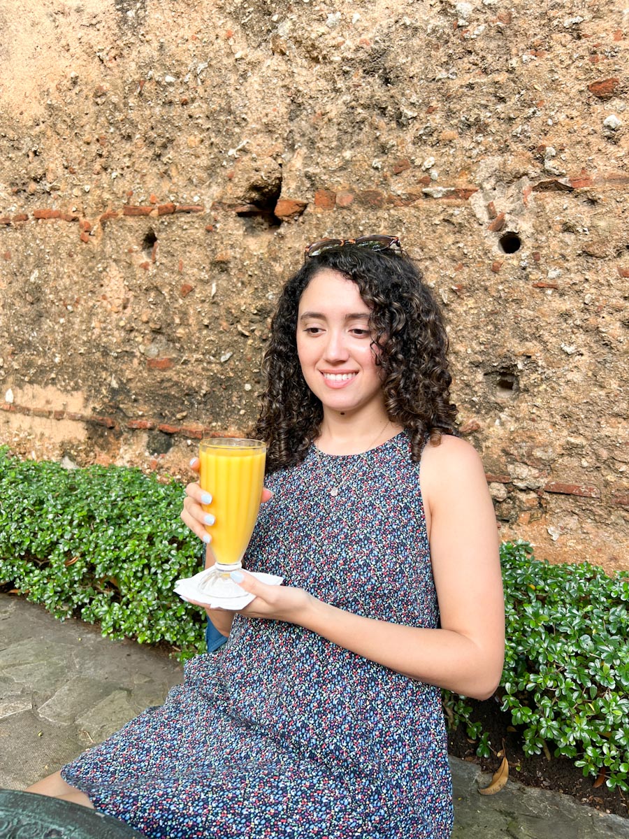 A woman sitting while holding a tall glass of fresh mango juice