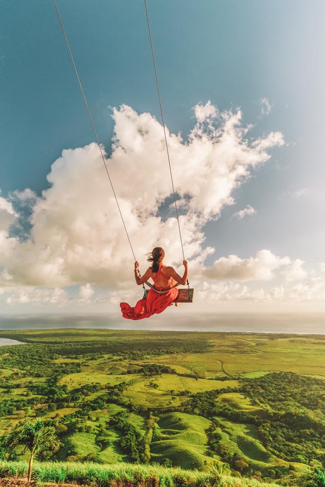 A girl in a dress swinging over mountains.