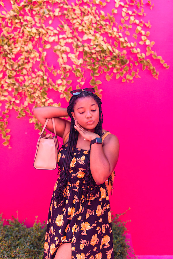A woman posing under a tree with a pink wall in the background.