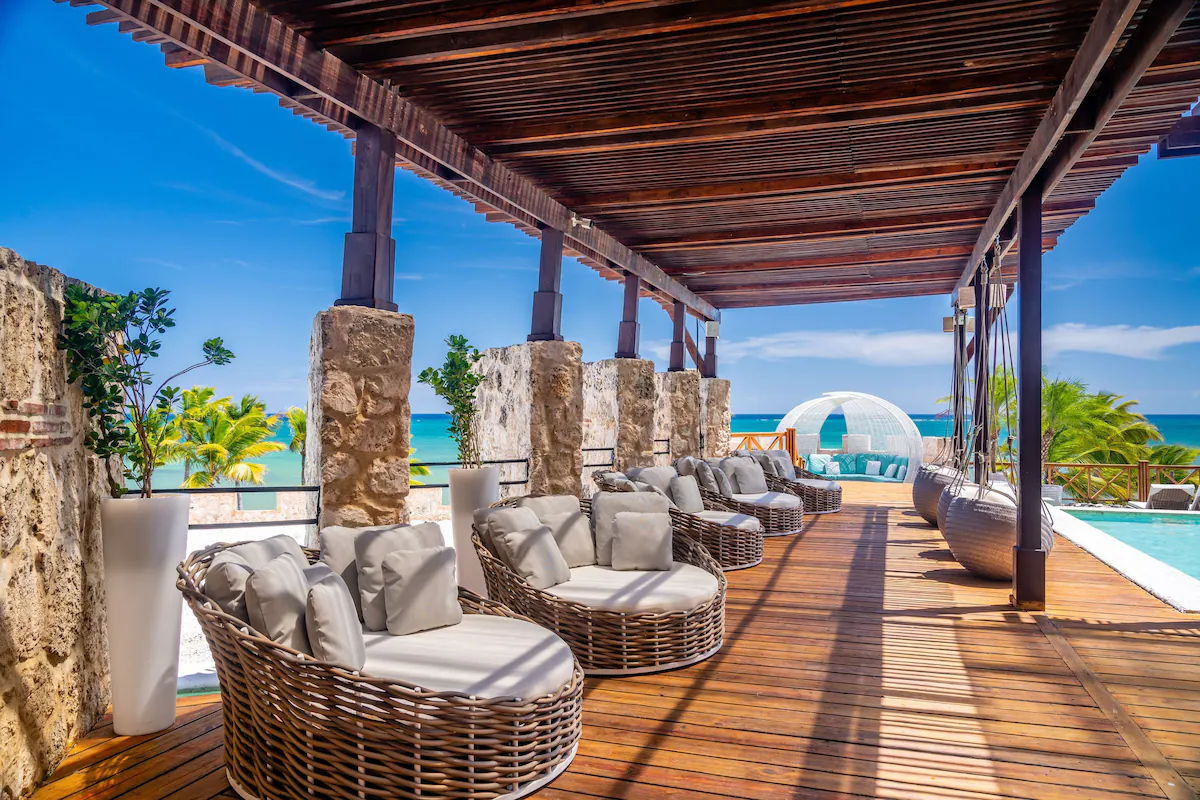 The outdoor lounge of a resort in the Dominican Republic with chairs, swimming pools, and a view of the sea.