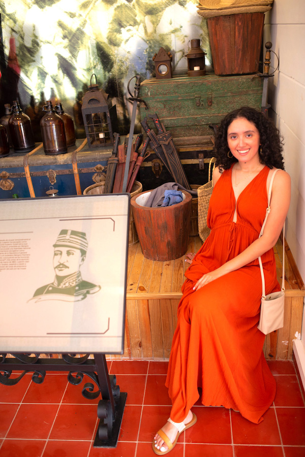 A woman in red dress sitting beside artifacts at Museo Gregorio Luperon.