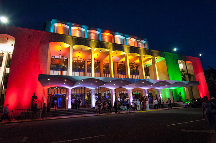 The outside of Teatro Nacional Eduardo Brito with multicolor lighting and surrounded by people.