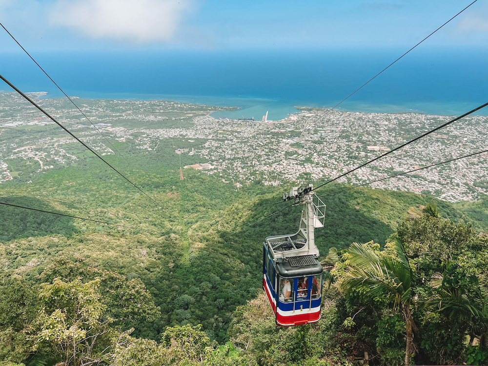 Cable car over trees, city, and sea.