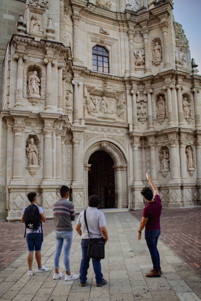 People with a tour guide looking at a Oaxaca City building architecture.