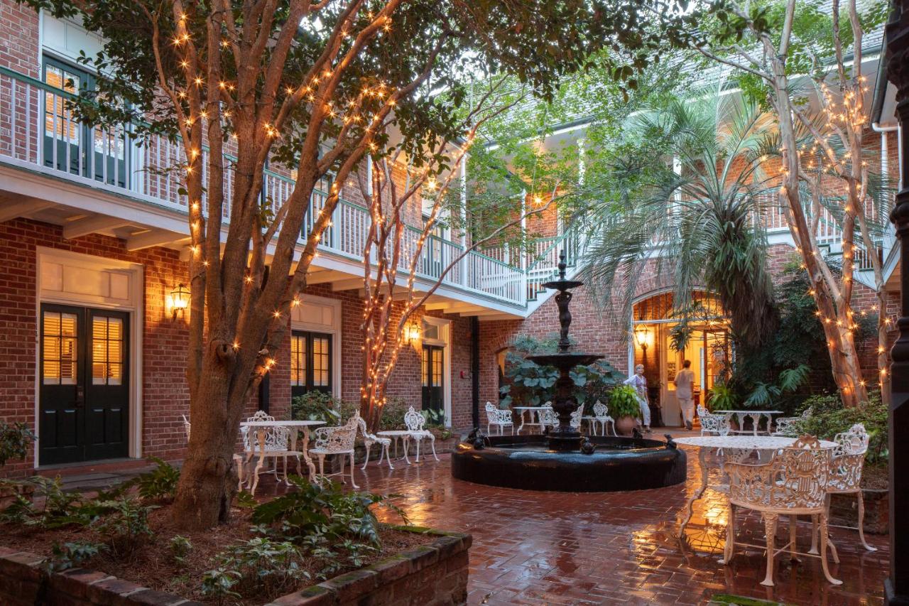 A courtyard of a hotel with fountain, metal chairs and tables, and trees adorned with decorative lights.