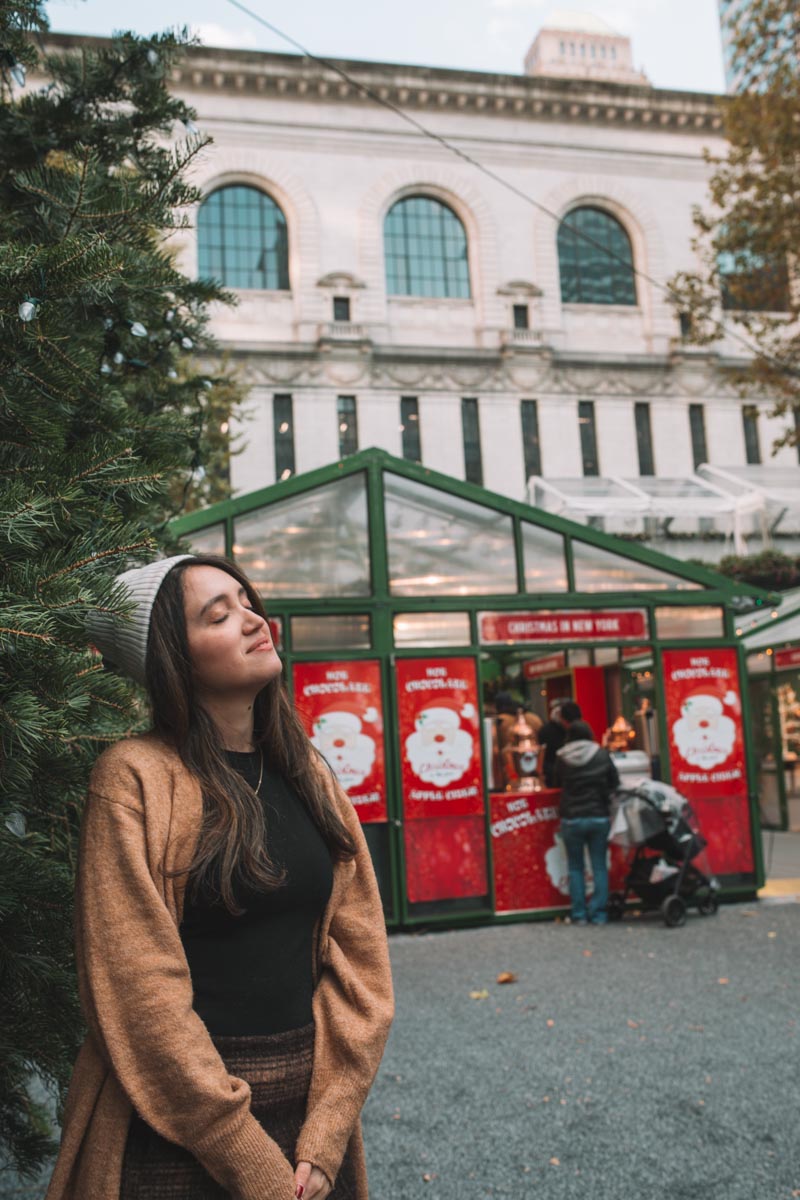 A woman standing beside a Christmas tree at Bryant Park Winter Market