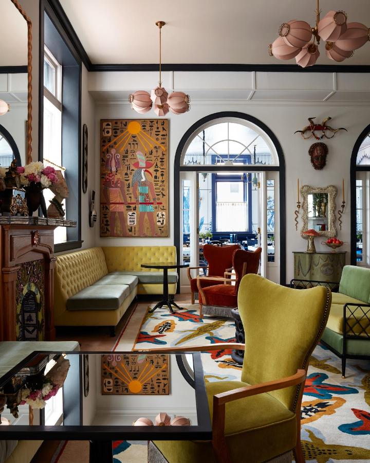 Carpeted sitting area of a boutique hotel in New Orleans with tables, chairs, couch, and artworks.