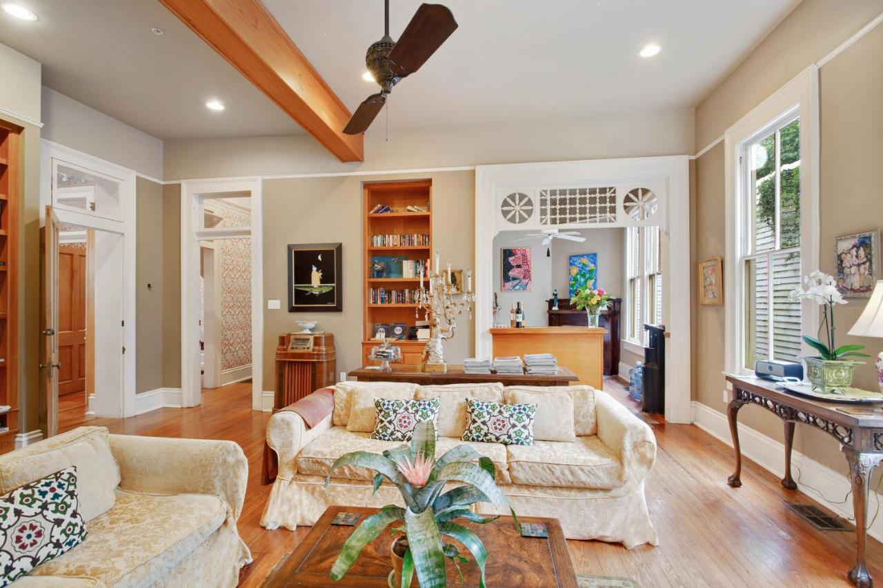 A living room at a New Orleans bed and breakfast with couches, tables, plants, bookshelves, and artworks.