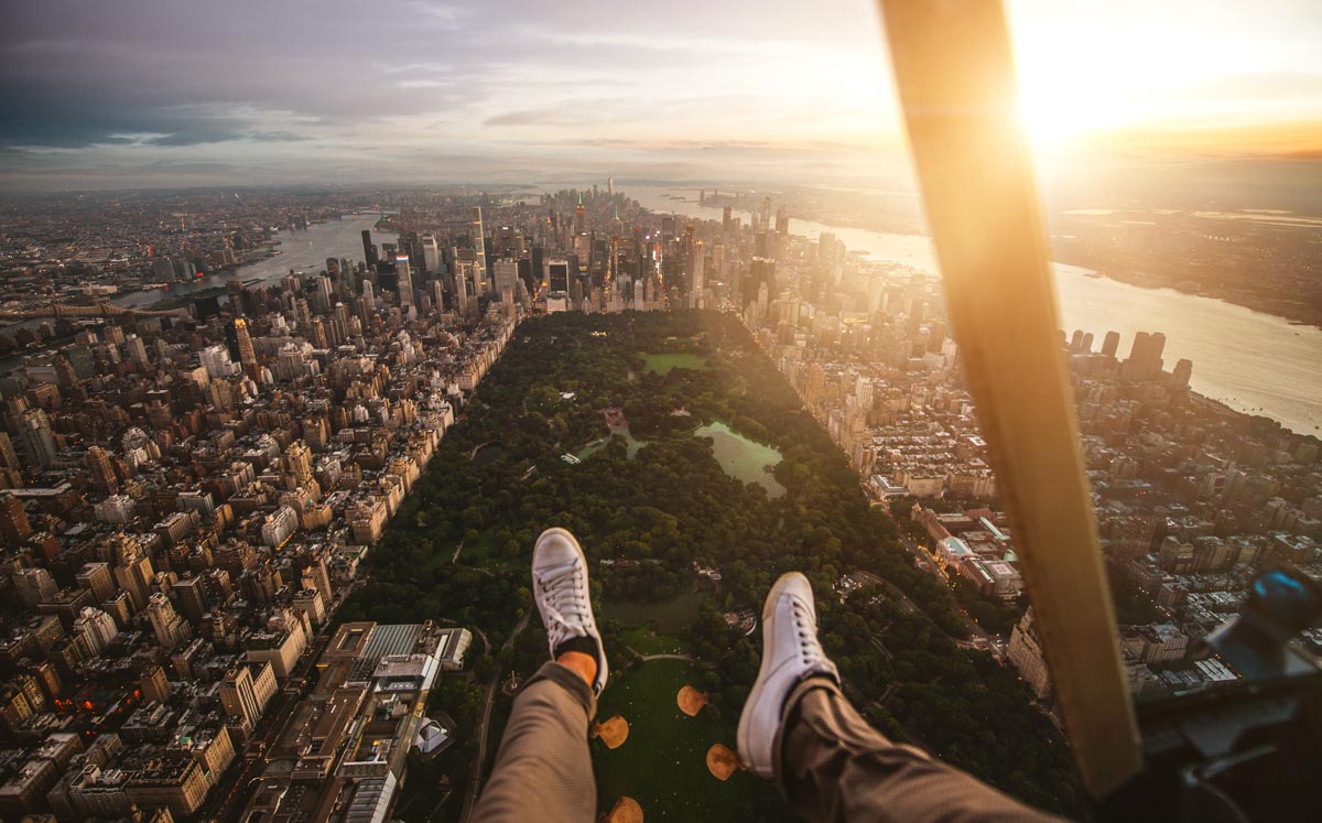 helicopter ride over nyc in august of a man's feet hanging over the sunset of nyc city views