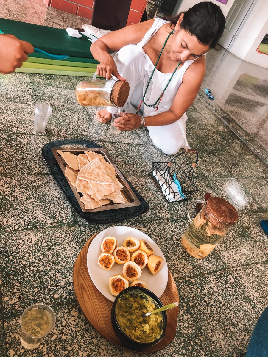 A woman pouring drinks from a pitcher to a plastic cup and with food, including chinola, presented on the floor