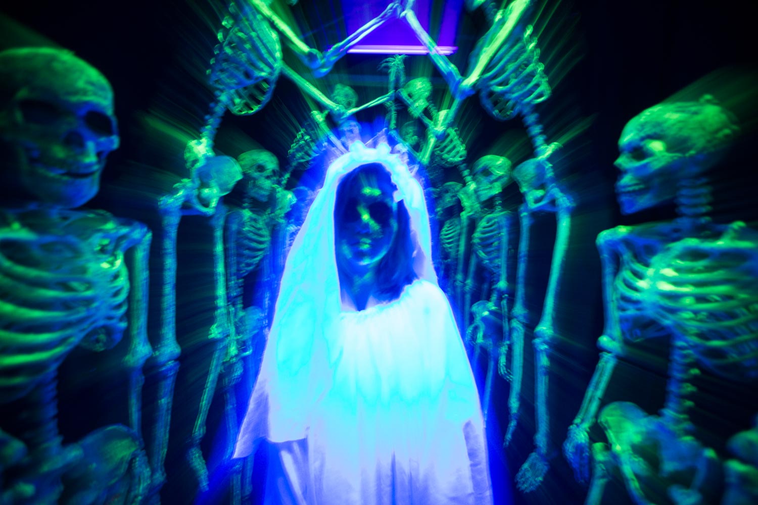 A figure of a woman in white surrounded by skeleton figures in a haunted house