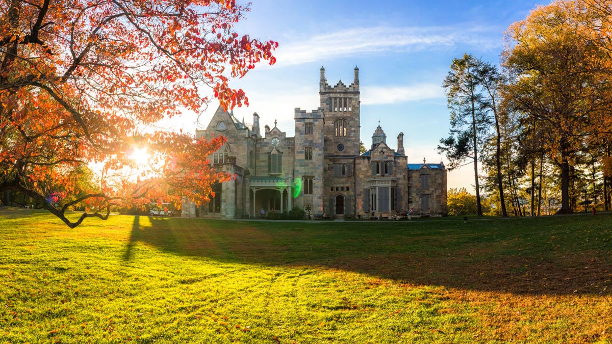 The front of Lyndhurst Castle in fall surrounded by trees with green, yellow, and red leaves