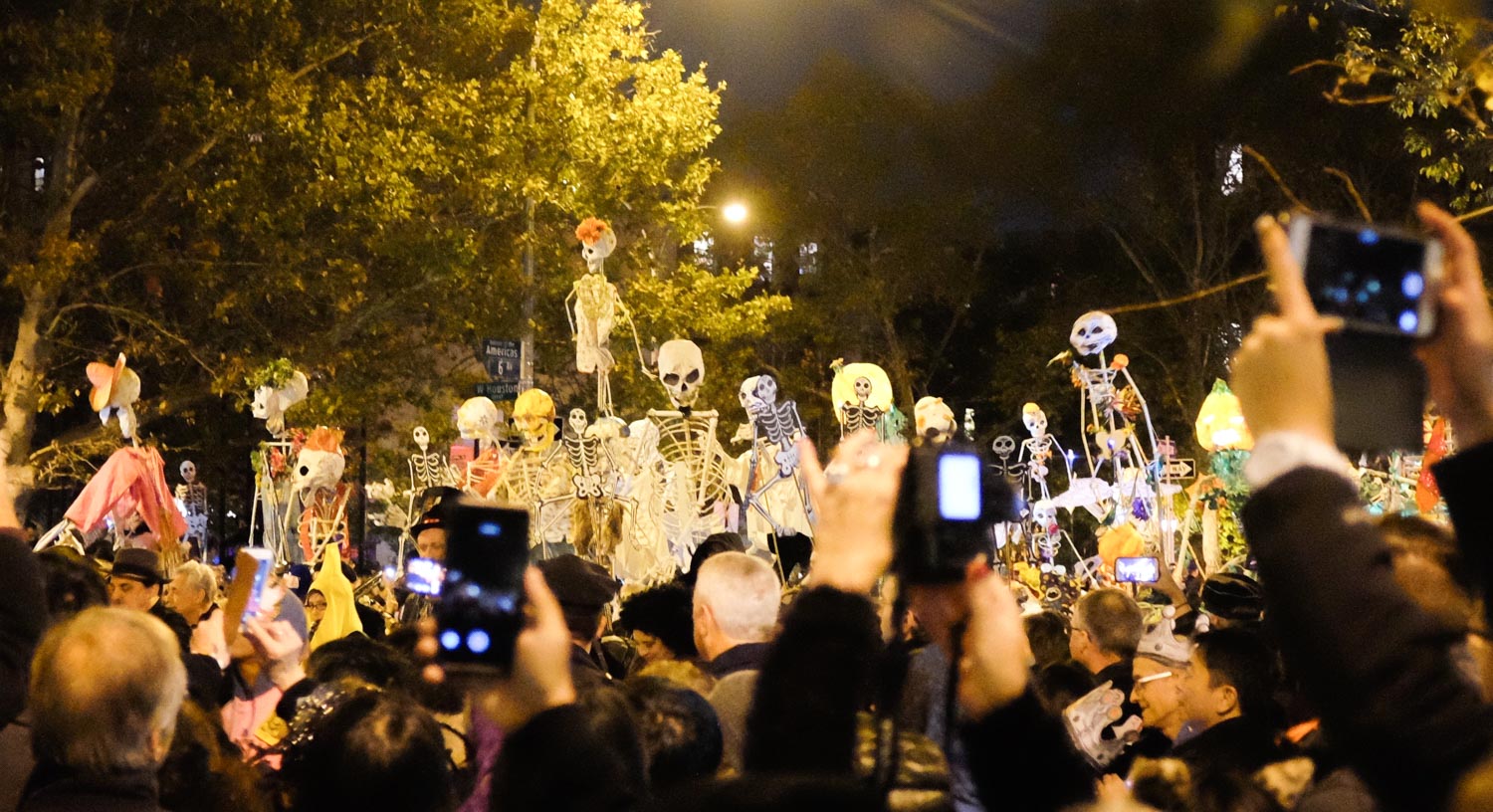 Fake skeletons being photographed by attendees at a halloween parade in New York City at night