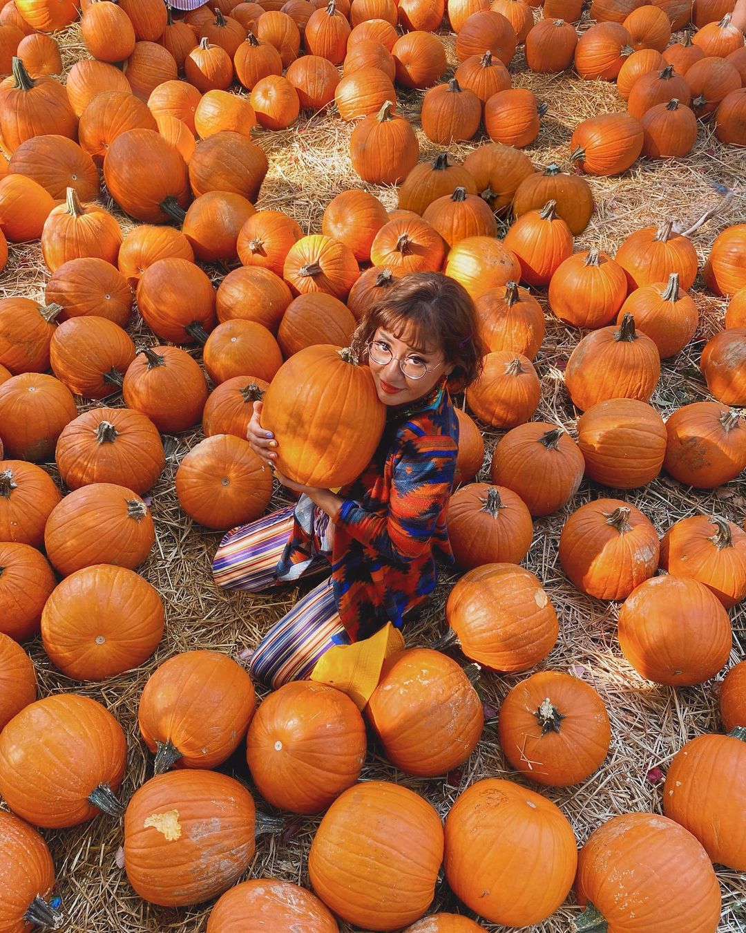A girl surrounded by pumpkins and holding one at Queens County Farm Museum New York in fall