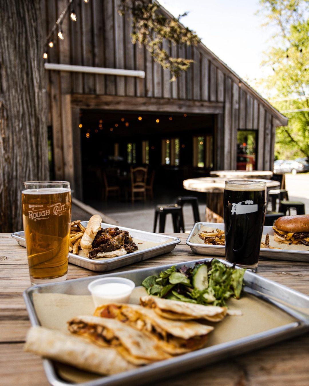 A table of food and drinks at Rough Cut Brewing in New Paltz with a wooden building in the background