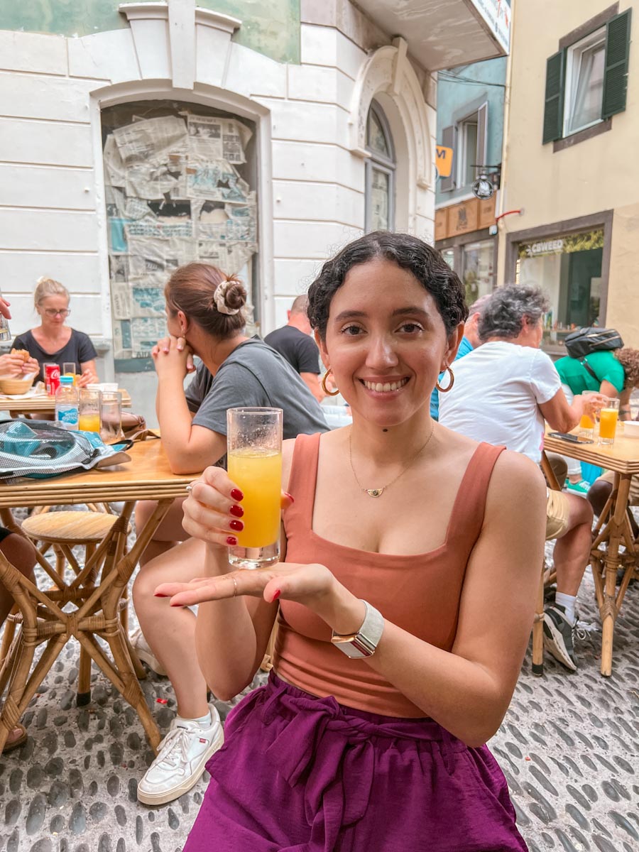 A woman dining on a street in Madeira and holding a glass of poncha