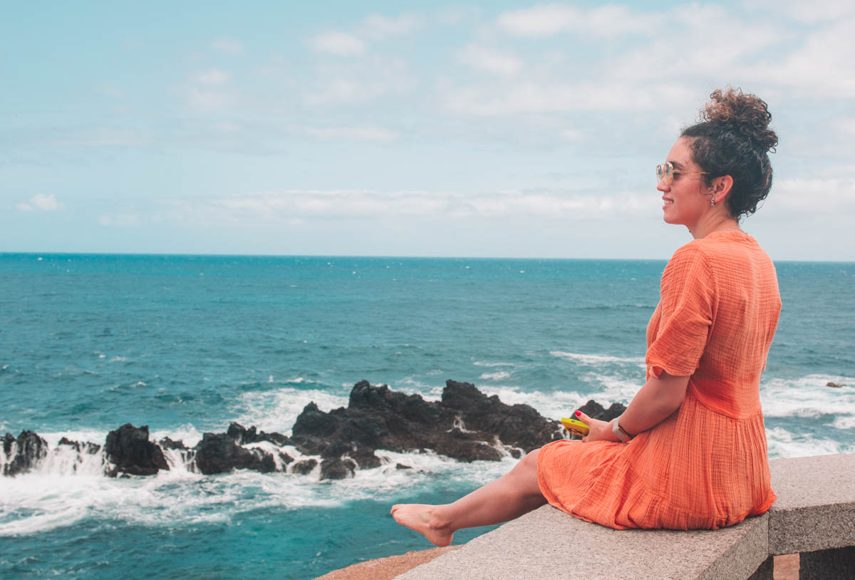 A woman in orange dress sitting and looking at the sea in Porto Moniz, Madeira, Portugal