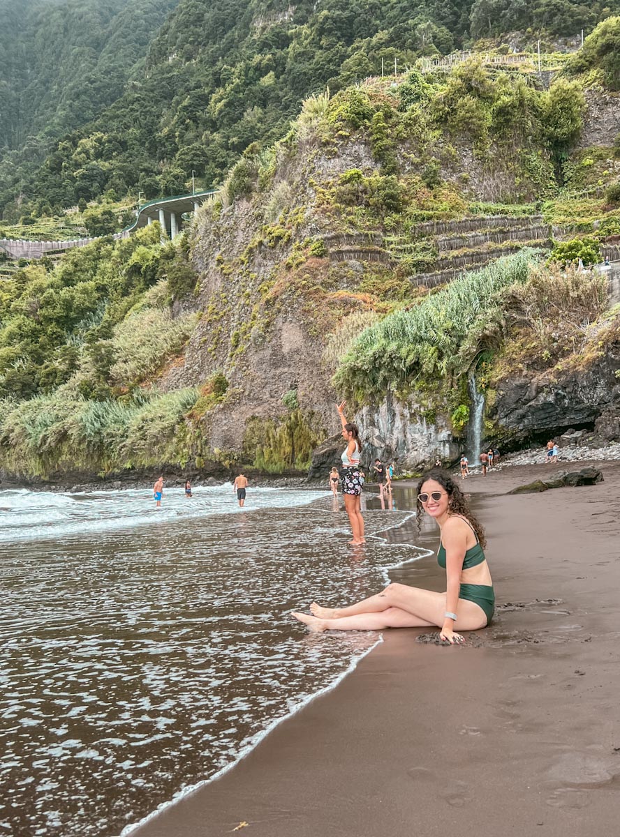 A woman sitting on Seixal black sand beach
