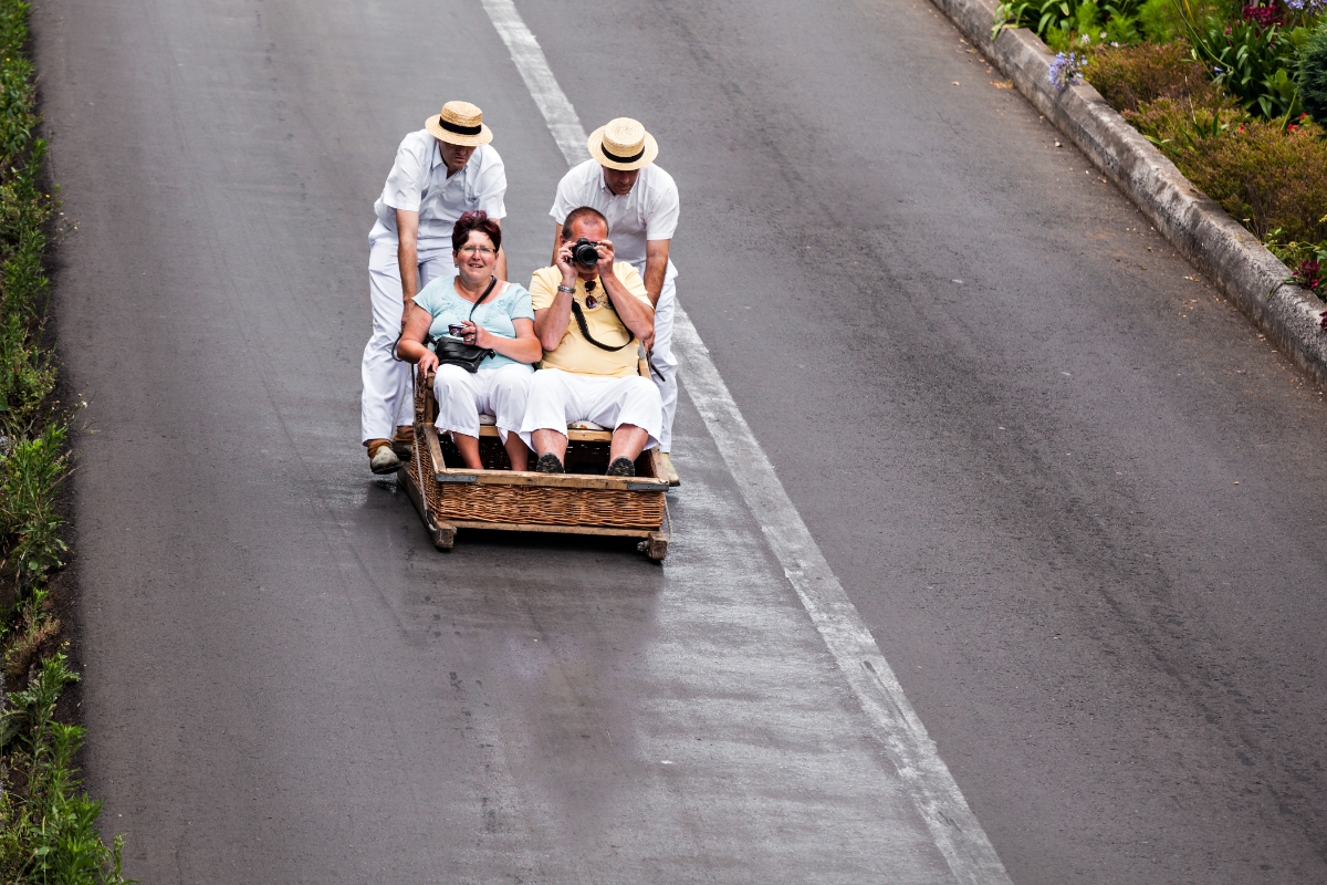 A man and a woman with cameras riding on a toboggan, which is being pushed by two men