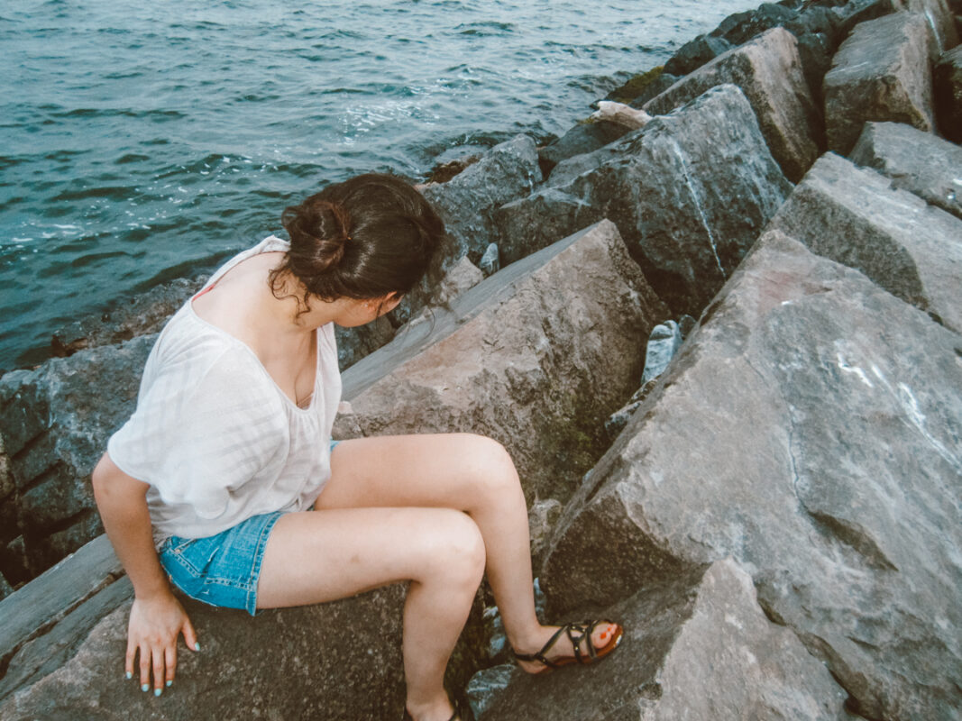 A woman sitting on the rocks by the sea near the H. Lee White Maritime Museum