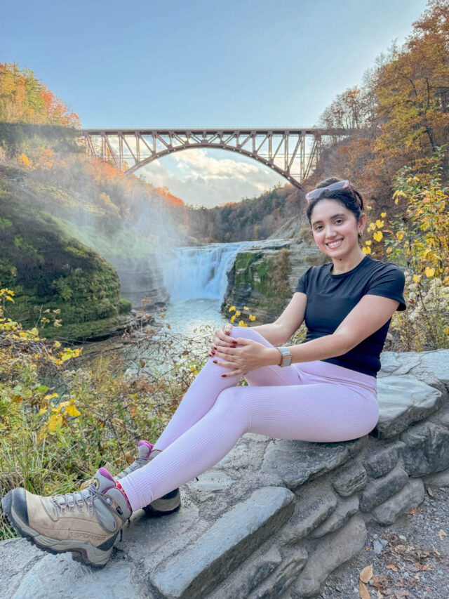 A woman sitting on a rock with a waterfall in the background at Letchworth State Park.