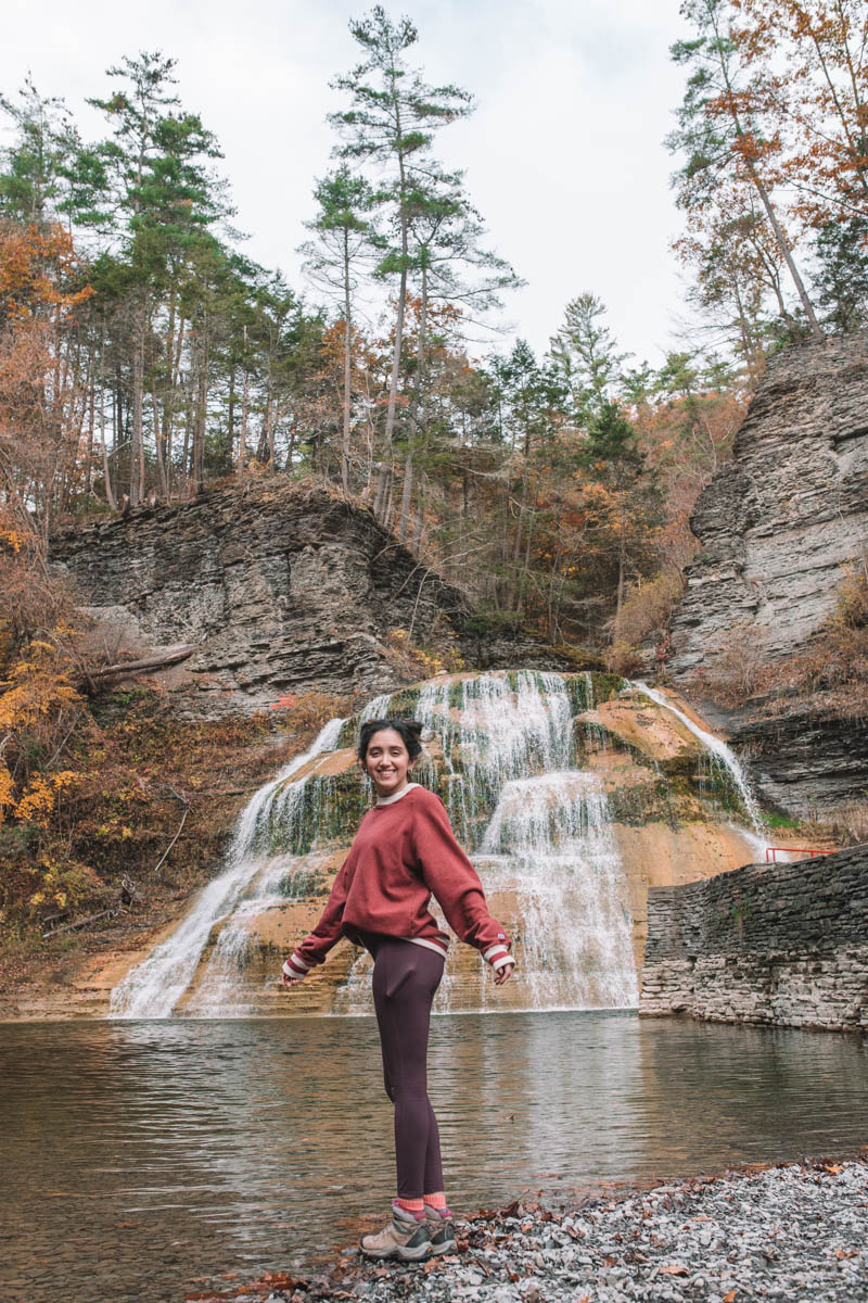 A woman standing in front of Lower Falls at Robert Treman State Park in fall.