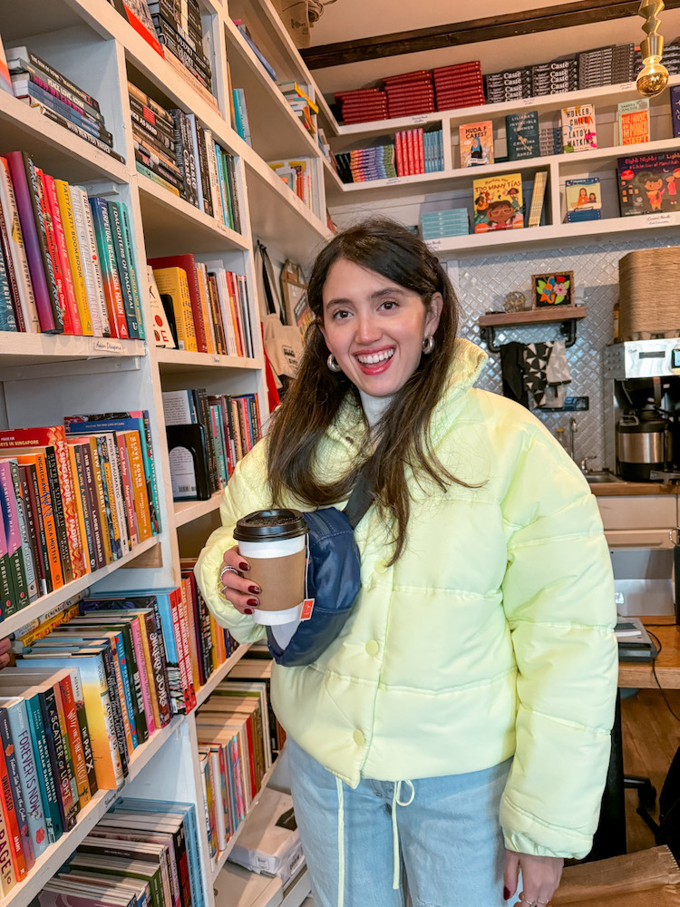 A woman holding a cup of coffee while browsing the shelves of a bookstore in New York City