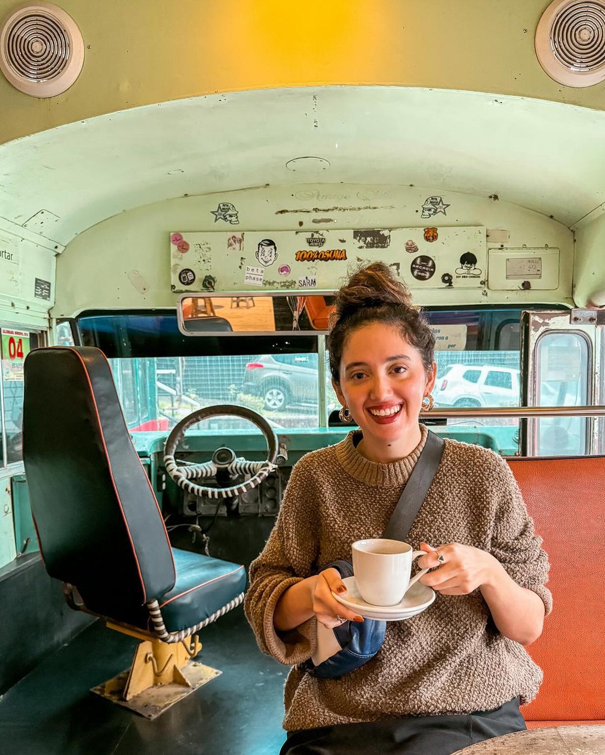 A woman holding a cup of coffee in a cafe with a vehicle-like interior