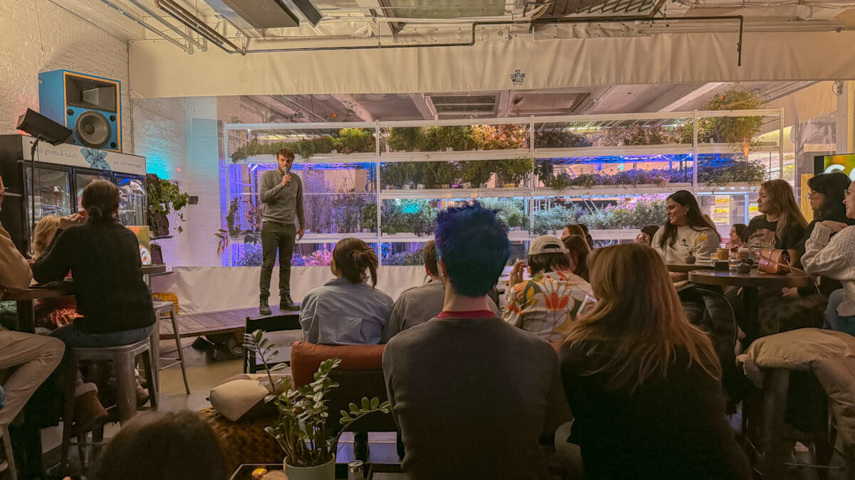 A man speaking to a group of people, with plants in the background
