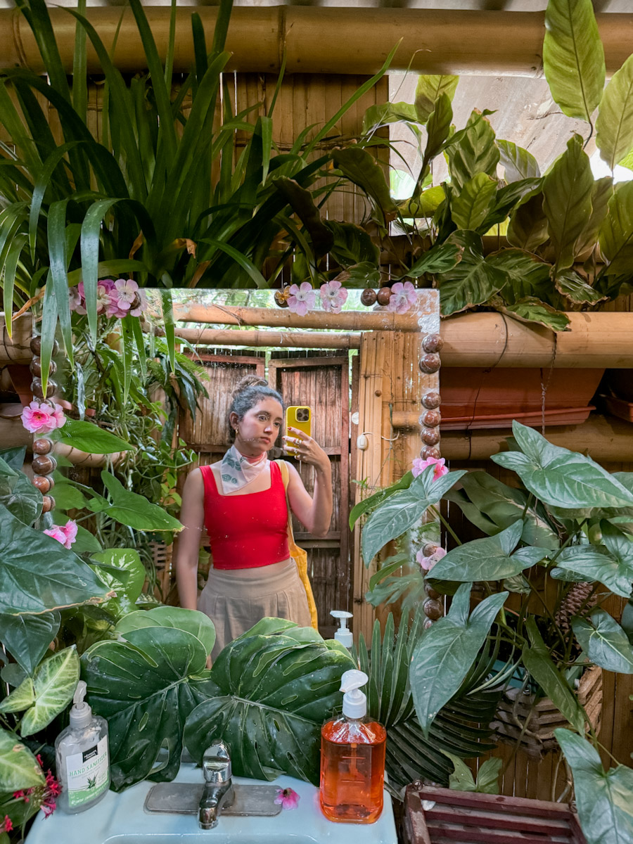 A woman taking a mirror picture of herself surrounded by plants.