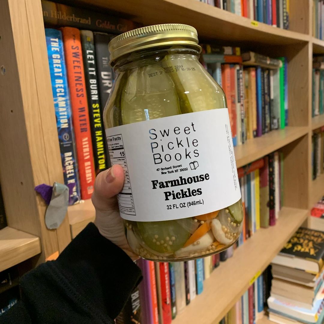 A jar of pickles with bookshelves in the background.
