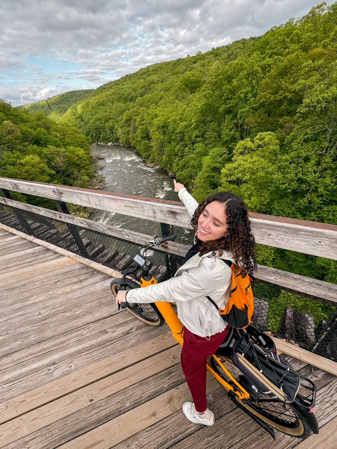 A woman on a bike pointing on a river in Laurel Highlands Pennsylvania.