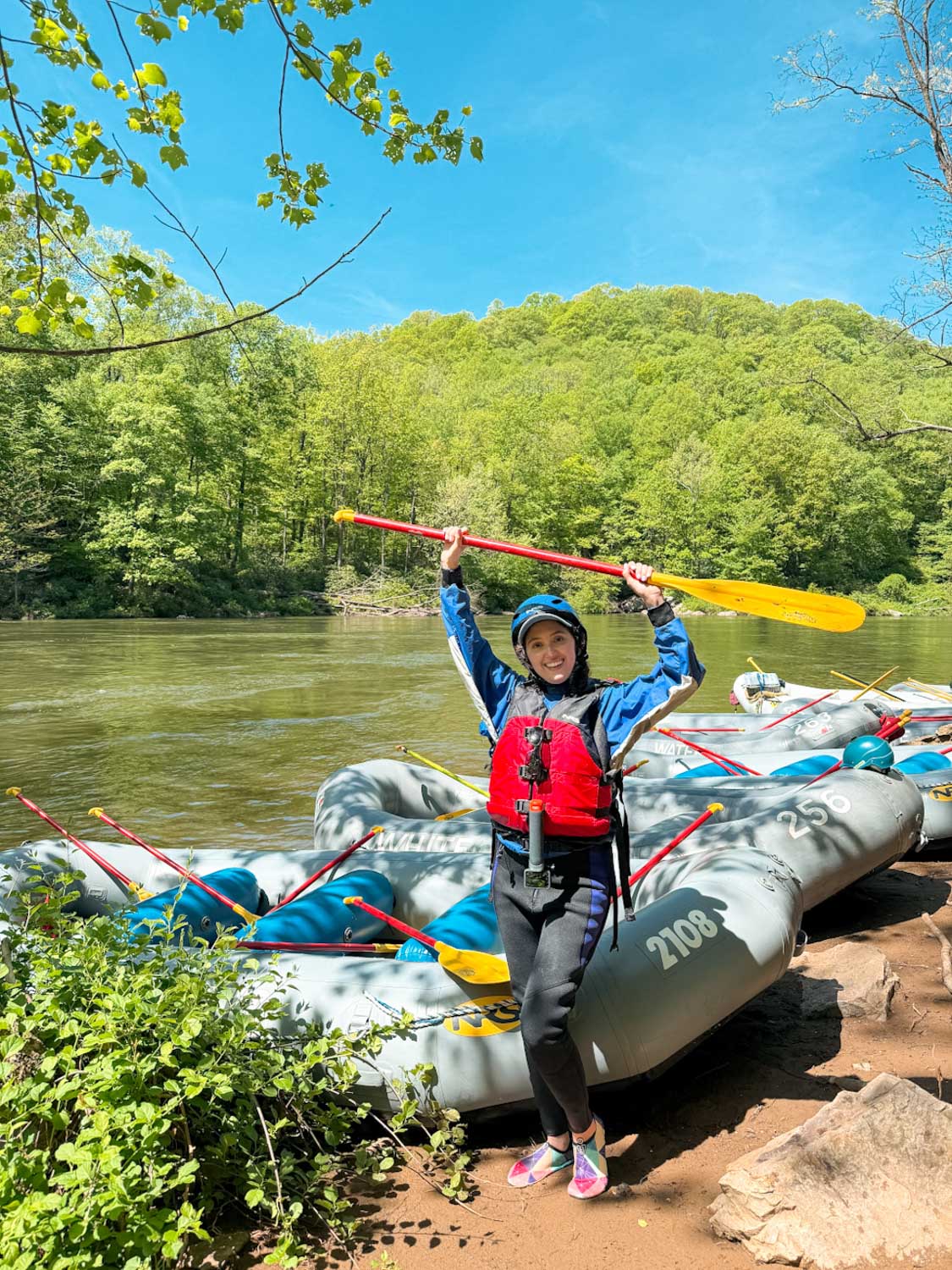 A woman standing near rafting boats and holding a paddle by a river at Laurel Highlands, Pennsylvania.