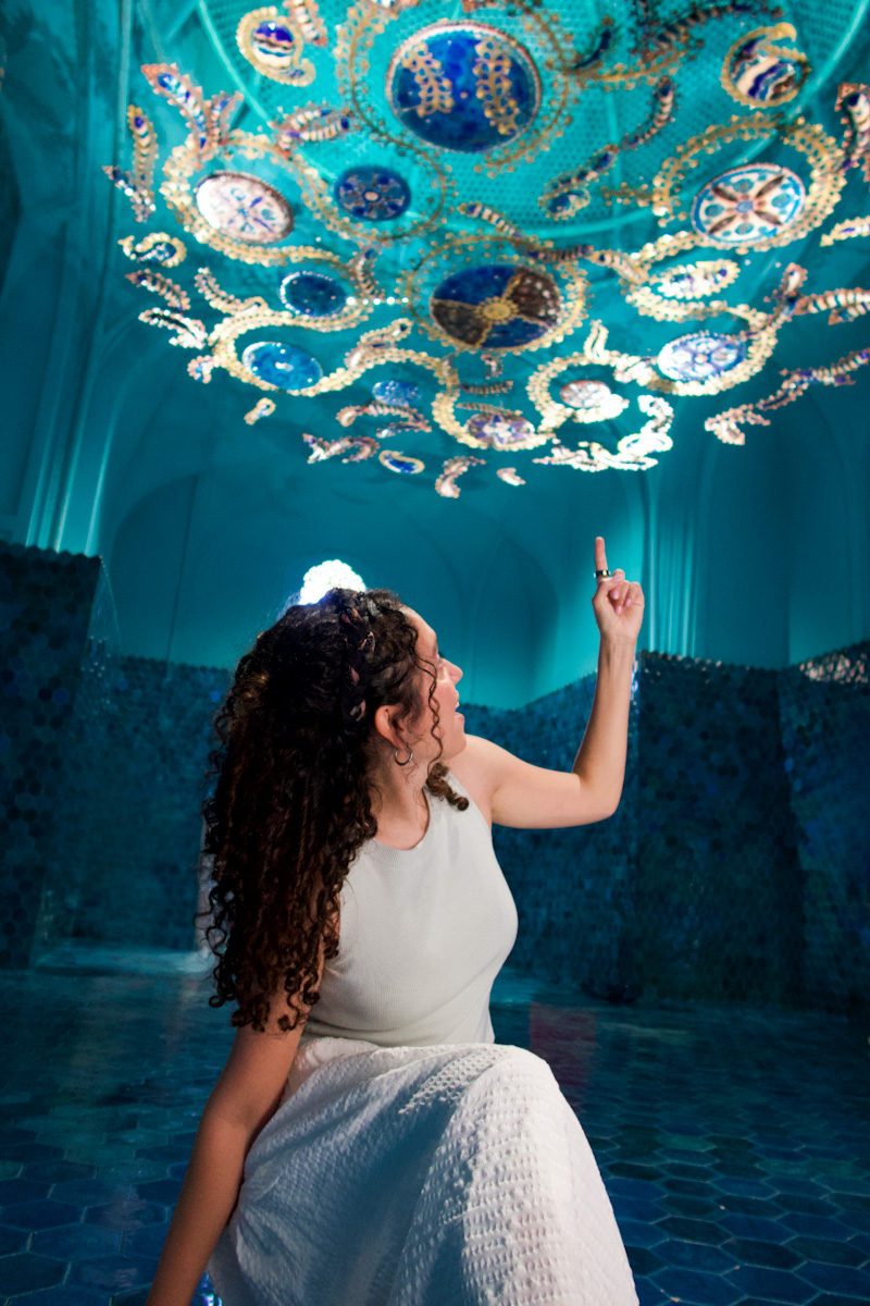 A woman standing below an art chandelier inside a blue room in Bukhara, Uzbekistan.