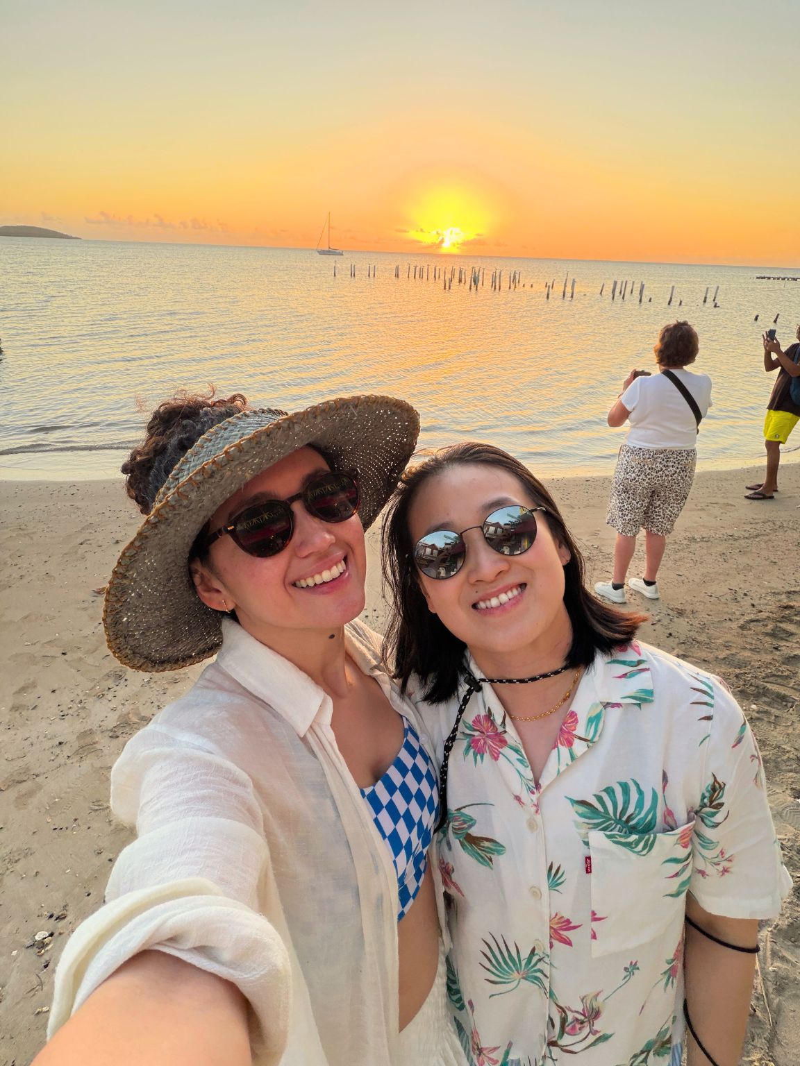 Two women dressed in summer clothes taking a selfie with the beach and sunset in the background in Puerto Rico.