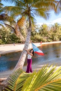 A woman holding on a palm tree with a Puerto Rico flag by a river.