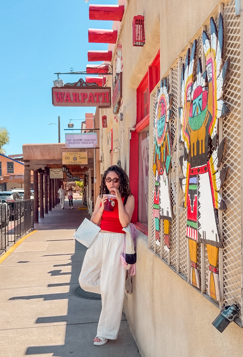 A woman drinking from a cup leaning against a street wall in Albuquerque, New Mexico.